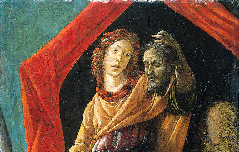 A delicately-featured woman with curly brown hair just shy of shoulder length looks at a man's severed head in her hand with a wry expression.